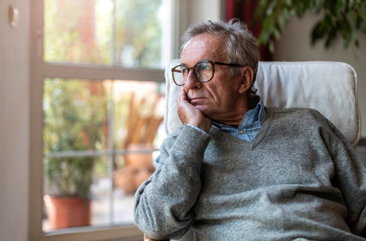 Screenshot 2026-06-17 at 104041 AM - HWK Law Group - HWK Law Group Older man with gray hair and glasses sits in a chair, gazing out a window in thought.