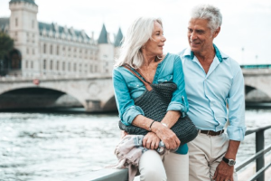 Screenshot 2026-08-17 at 15311 PM - HWK Law Group Older couple strolling along a riverside promenade, smiling at each other with a historic bridge in the background.