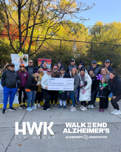 Untitled design - HWK Law Group Group of people posing with a large ceremonial check at a Walk to End Alzheimer's event, autumn trees in the background.